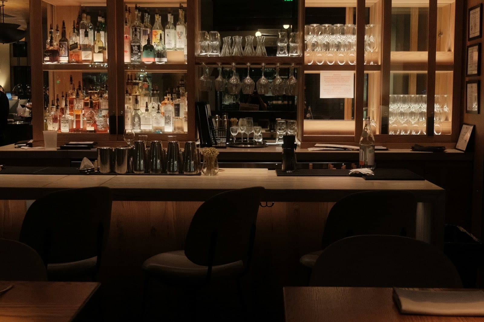 An empty bar before service, with lit bottles and glassware on the back shelves